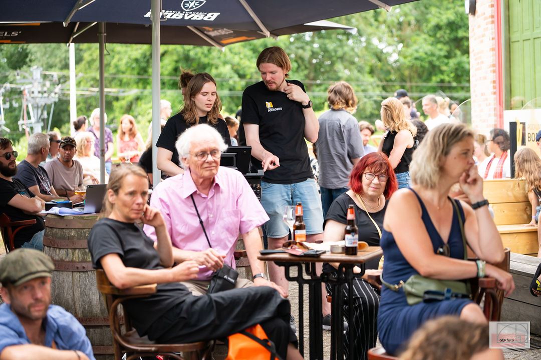 Bezoekers zitten samen aan tafeltjes op het festivalterras in de zon — foto: GEKfoto