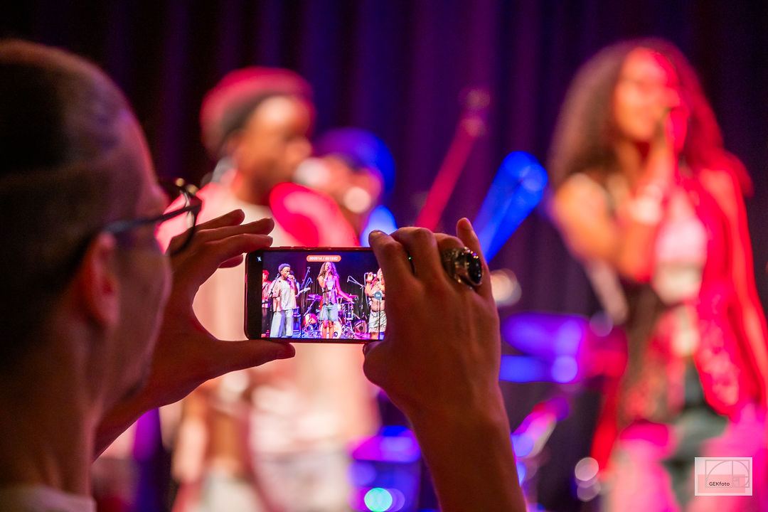 Bezoeker filmt het optreden met de telefoon, het podium kleurt op de achtergrond — foto: GEKfoto